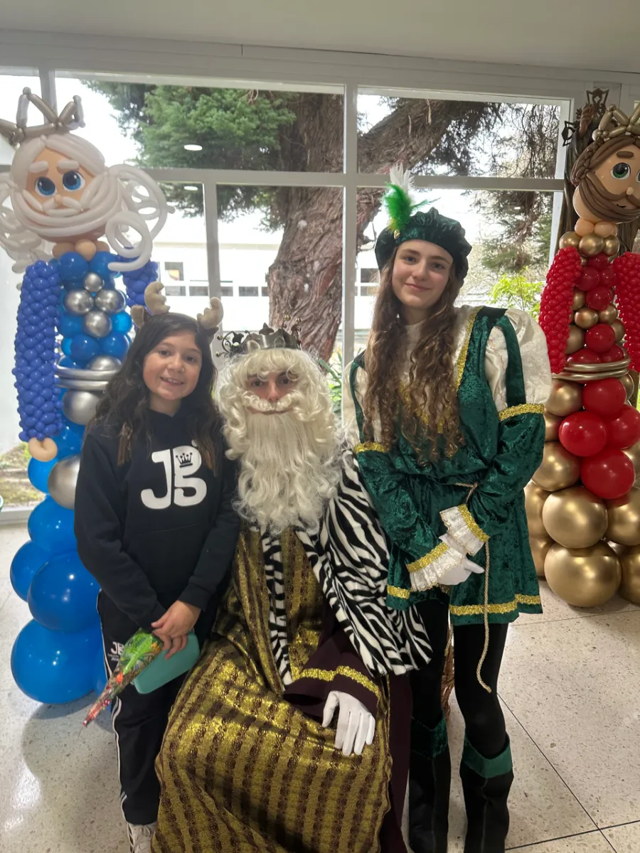 Una alumna y un paje posan junto a un Rey Mago en el vestíbulo del colegio, decorado con figuras de globos