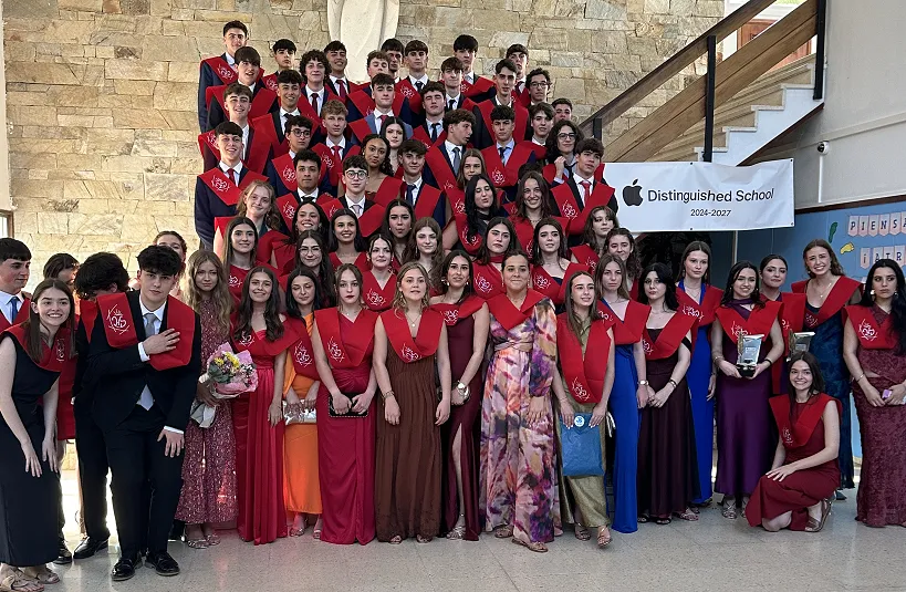 Foto de familia de la promoción de Bachillerato con las bandas rojas de graduación, bajo el cartel de Apple Distinguished School