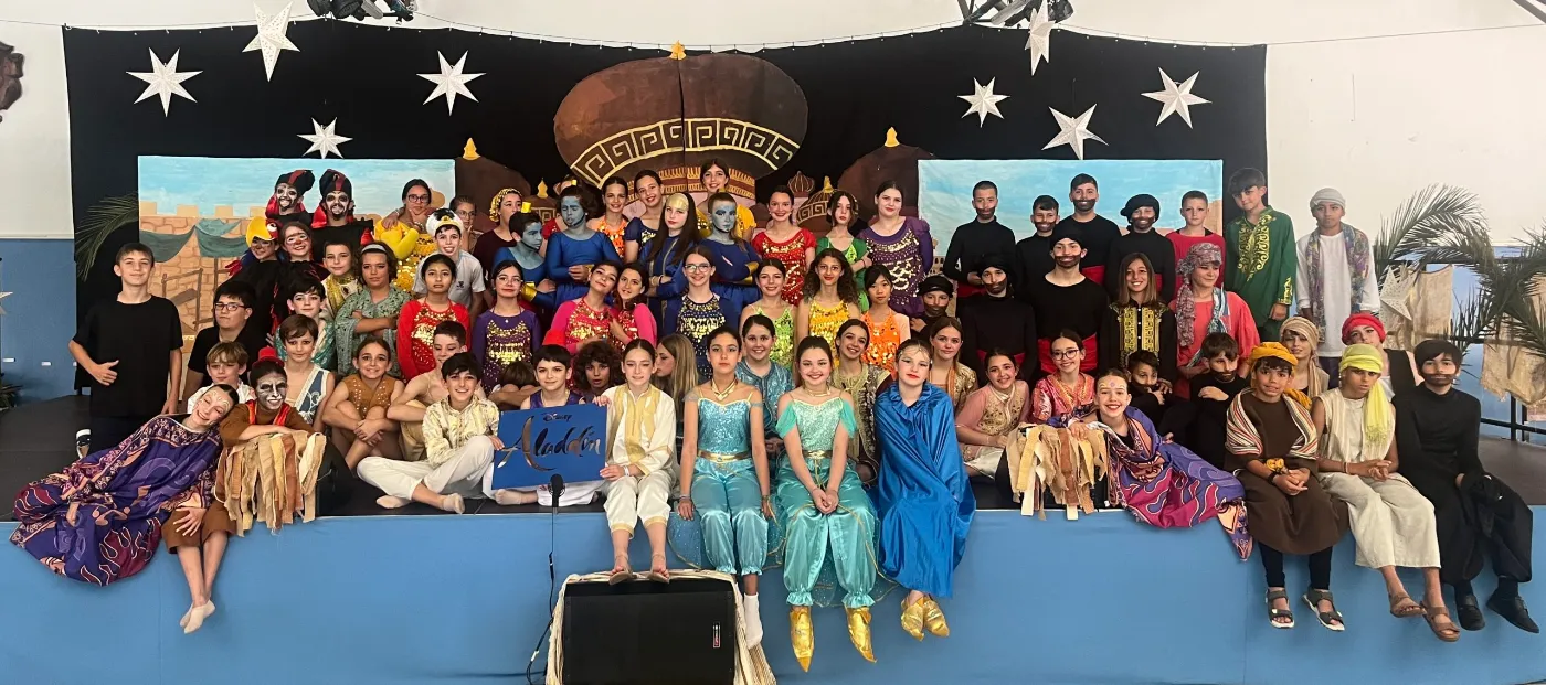 Todo el reparto del musical de Aladdín posando en el escenario con sus trajes, ante el decorado de la lámpara y las estrellas